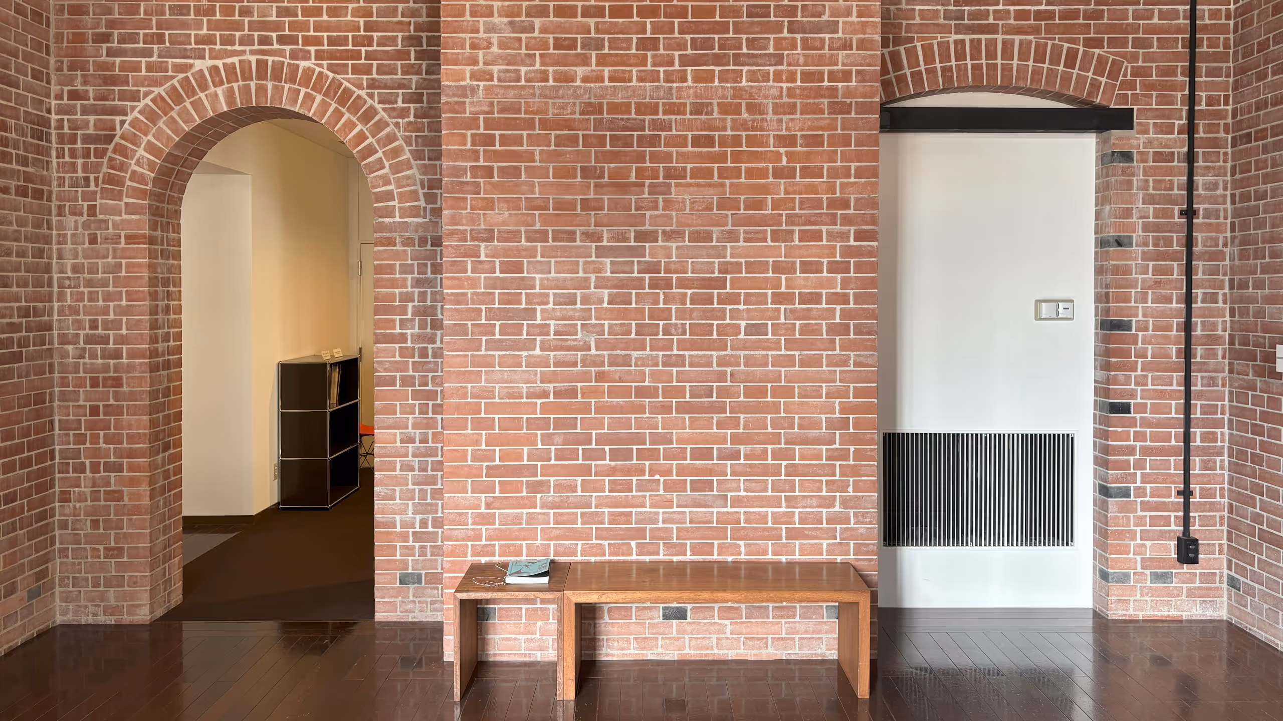 レンガで作られた壁は左右にアーチ付きの出入り口がある。その間は少し手前にせり出しており、そこに寄せて木製のベンチが並べられている。ベンチには表紙が青い展覧会の図録が置かれている。