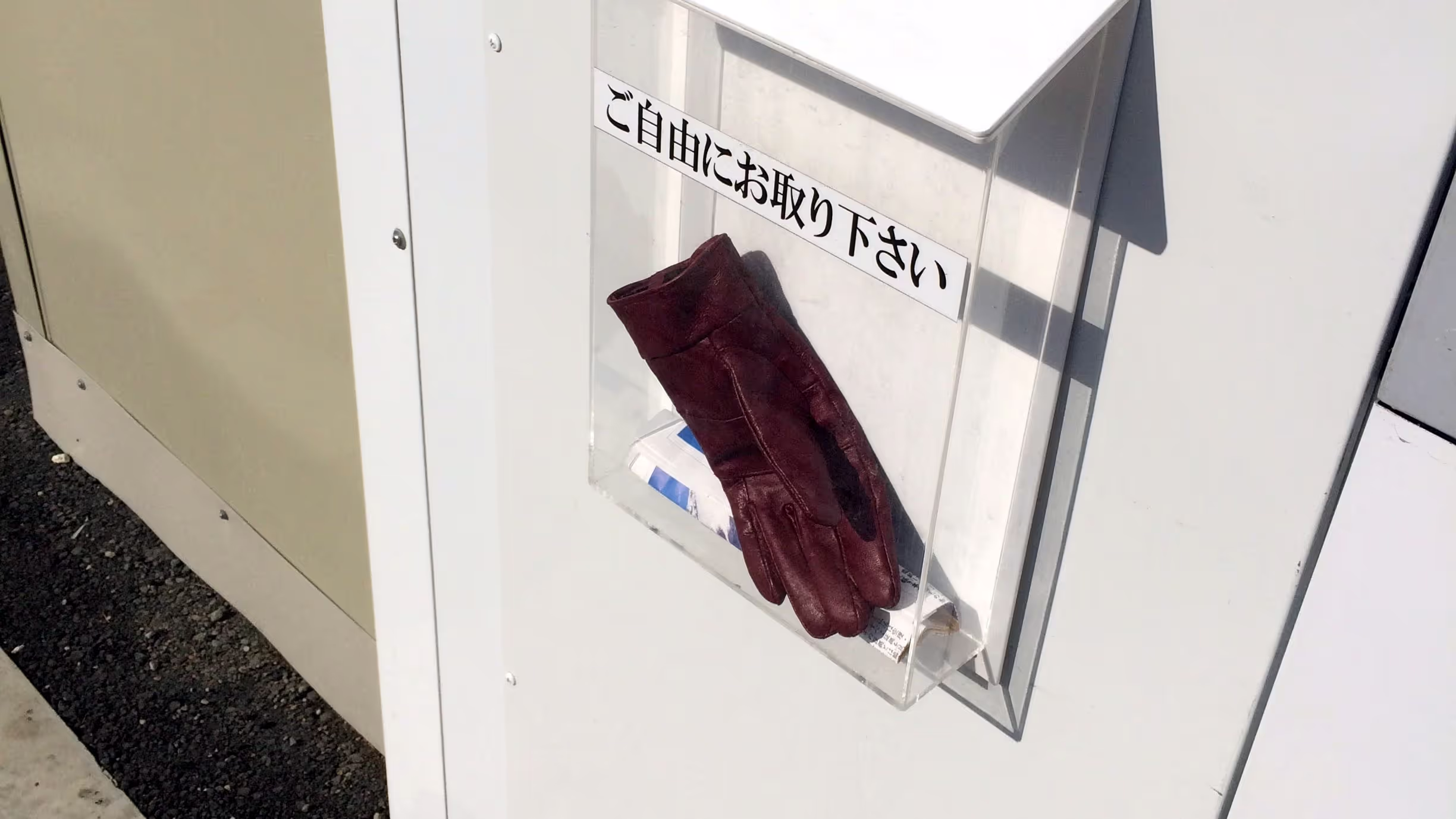 マンション建設現場の仮囲いに取り付けられている無料のチラシを配布するための箱に入れられたえんじ色の手袋。