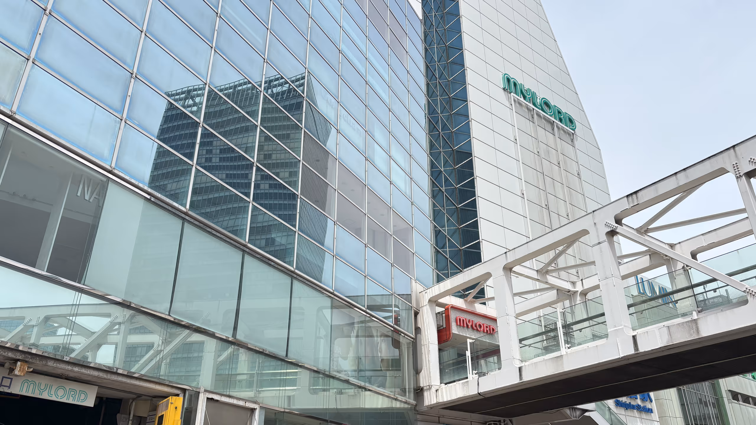 見上げると、ガラス張りのビルへ続く空中通廊の上やその隣のビルの壁面に、まだミロードのロゴが確認できる。