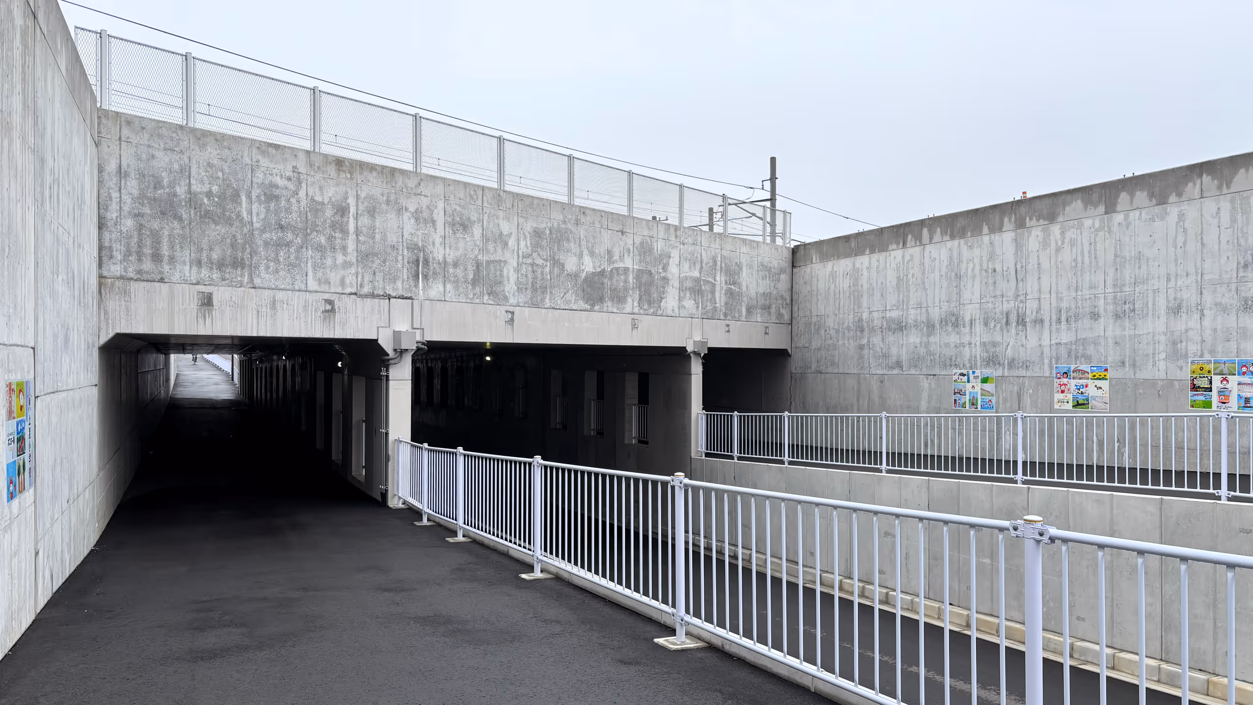 左右に歩道を備えた車道が、地面に潜るようにぶ厚いコンクリート造りで固められて通っている。上にはJR相模線の電線が見える。